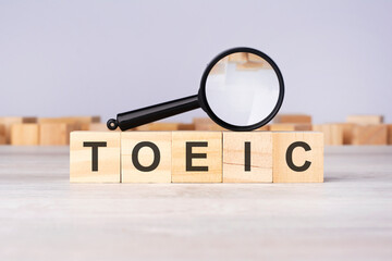 Poster - woden blocks with a magnifying glass text: TOEIC. Test Of English For International Communication