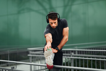 Wall Mural - Young man stretching hands before jogging in sports clothes and headphones on his head