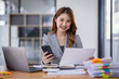 © David - Smiling young Asian business woman executive looking at smartphone using cellphone mobile cell tech, happy ethnic professional female worker working in office typing on cellphone sitting at desk.