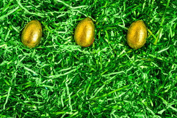 Wall Mural - Three gold foil wrapped chocolate easter eggs in a nest of easter grass, as a holiday background
