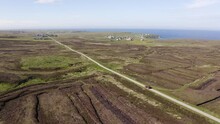 Tilting Drone Shot Of A Peat Cutter Driving His Tractor Full Of Peat Home Near His Peatland. Filmed On The Moorland Surrounding Ness On The Isle Of Lewis, Part Of The Outer Hebrides Of Scotland.