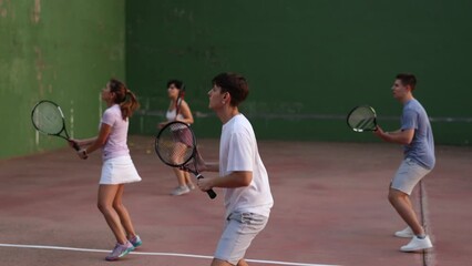 Wall Mural - Group of sporty young frontenis player swinging string racquet to hit ball on outdoor walled court on sunny summer day. Sport and active lifestyle concept