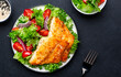 Fried cod fish with salad garnish from lettuce, cherry tomatoes and red onion with sesame seeds, black table background, top view