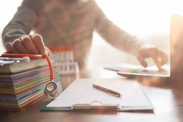 Male doctor search information in book and writtnig prescription, medical stethoscope on the desk at clinic. Medical knowledge and education concept.