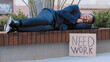 © Yuliia - Sleeping homeless fired African American man in city tired with searching job relax on bench. Male sleep outdoors with poster need work. Illegal ethnic guy lost job poor jobless unemployment racism