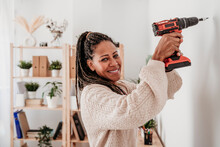 Smiling Woman Using Drill Machine On Wall At Home