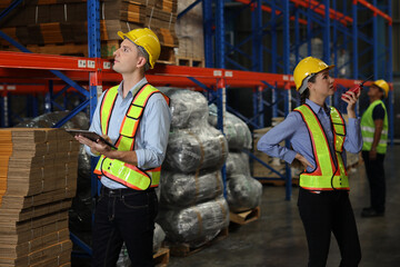 Group of warehouse workers with hardhats and reflective jackets using tablet, walkie talkie radio and cardboard while controlling stock and inventory in retail warehouse logistics, distribution center