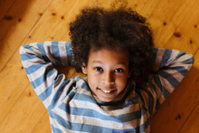 Smiling Boy With Hands Behind Head Lying On Floor At Home