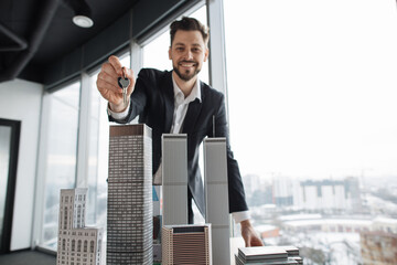 Focus on keys in hand of real estate manager homeowner businessman banker salesman caucasian successful man sell house property from new apartment near 3d city model at office with panoramic window