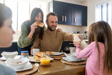 Happy Man And Woman Having Breakfast With Children In Kitchen