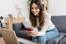 Happy Young Woman Using Smart Phone Sitting On Sofa At Home