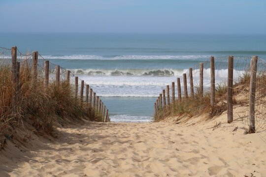 chemin de sable cloturé par une ganivelle et descendant vers la mer et la plage des dunes à lège cap