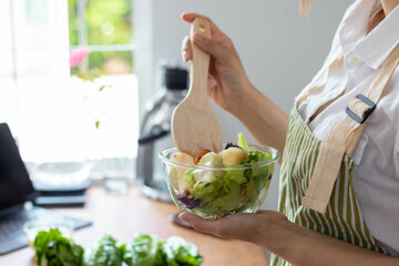 young woman is making salad from vegetables she has prepared on table in her home kitchen to get salad that is clean and safe because ingredients are carefully selected. healthy food preparation ideas