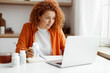 © shurkin_son - Pretty young mother ordering organic food supplements from marketplace or online pharmacy, sitting at kitchen table with copy book and bottles of vitamins, holding plastic jar of omega 3 fatty acids