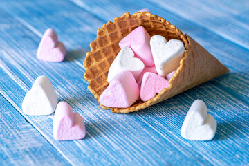 Wall Mural - Waffle cone with heart-shaped marshmallows, close-up on a blue wooden background.