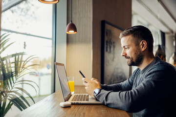 Wall Mural - a busy digital marketer is sitting in coffee shop and working on social media by using phone and lap