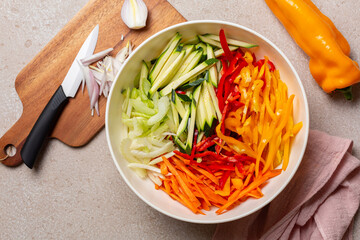 Cutting fresh raw , vegetables, onion, julienne carrot, bell peppers, zucchini, celery.  Knife, wooden board. Top view.