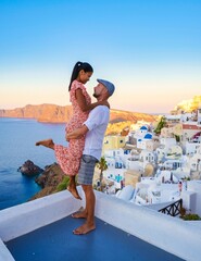 Wall Mural - Couple watching the sunset on vacation in Santorini Greece, men and women visit the Greek village of Oia Santorini.