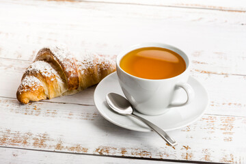 Poster - Breakfast with cup of tea and croissant on wooden table.