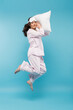 full length of barefoot young woman in night mask and sleepwear holding pillow and levitating on blue.