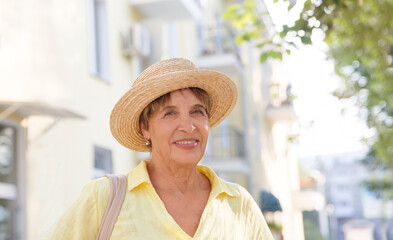 happy senior woman in sun hat walks  on summer city. 