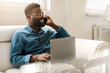 © Prostock-studio - Happy black businessman in glasses calling by phone, working with laptop on couch in office interior, free space