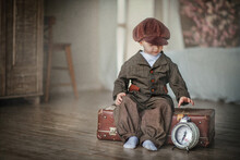 Portrait Of A Boy. Little Gentleman. The Boy Smiles. Handsome Little Boy. Boy In A Vintage Suit. The Kid Is Sitting On An Old Suitcase. Near The Clock. Boy In A Cap. Kid In A Hat