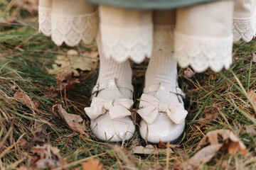 Cropped photo of child girl stylish canvas vintage style green dress with lace details, white shoes and pantyhose on nature autumn background. Photo for catalog. Beauty and fashion concept