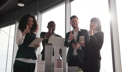 Wall Mural - Team of diverse four multiethnic businesspeople having meeting in boardroom at office with panoramic windows blurry cityscape standing near table with skyscraper building maquette showing thumbs up