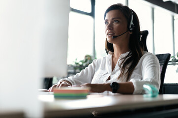 Canvas Print - Friendly smiling woman call center operator with headset using computer at office.