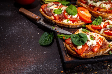 Wall Mural - Hot loaded pizza sandwiches with tomatoes, mozzarella cheese and pepperoni, on dark background with herbs, olive oil and spices