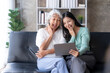 © amnaj - Happy Asian mother and daughter using tablet for video call at home on vacation.