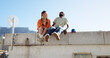 © Siphosethu F/peopleimages.com - Love, friendship and a couple sitting on rooftop of city building in summer time. Diversity, friends and romance, gen z urban dating for happy woman and black man with smile and skateboard on date.
