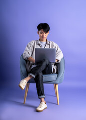 Wall Mural - full body image of young asian man using laptop on purple background