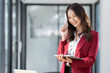© crizzystudio - Asian businesswomen or freelancers smiling near desks mobile phone tablet in the office wear fashion-style clothes Gather information about online jobs and exports.