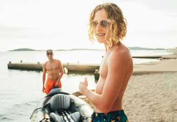 Wall Mural - Smiling long blonde hair teen in fancy sunglasses portrait while returning back from evening kayaking ride with father by Adriatic sea harbor. Vacation and family value vertical image.