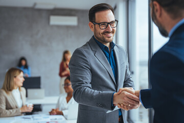 Portrait of cheerful young manager handshake with new employee. Business partnership meeting in office. Close up of handshake in the office. Mature businessman shake hands with a younger colleague