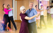 Smiling senior woman and man dancing slow ballroom dance during group class in choreography studio