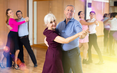 Poster - Smiling senior woman and man dancing slow ballroom dance during group class in choreography studio