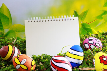 Poster - Easter eggs and blank notepad on green grass background with copy space
