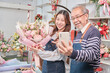 © tigercat_lpg - E-commerce business, senior Asian male florist worker and daughter show floral arrangements, online live streaming, selfie by smartphone application in bright flower shop, beautiful blossoms store.