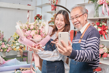 E-commerce business, senior Asian male florist worker and daughter show floral arrangements, online live streaming, selfie by smartphone application in bright flower shop, beautiful blossoms store.