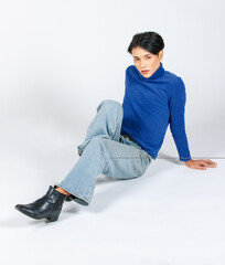 Wall Mural - Portrait isolated cutout studio full body Asian young sexy slim fashionable LGBTQ gay male model in turtleneck long sleeve shirt jeans leather boots sitting laying on floor posing on white background