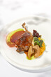 Traditional france dish - duck confit with baked apple on light background with shadows of sunlight. Roasted duck leg with fruits and gravy on white plate in summer dining Elegant roasted leg