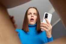 Shocked amazed Caucasian woman unpacking box and looking in cardboard box with open mouth and big eyes holding mobile phone in hands, received damaged item, view from the inside of package.