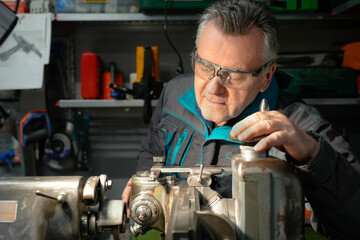 Wall Mural - A man in safety glasses and work uniform sets up a grinding machine in his workshop. The grinding machine details in focus. In the background are various working tools on metal shelving for workshop