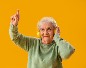 Canvas Print - Senior woman in headphones pointing at something on yellow background