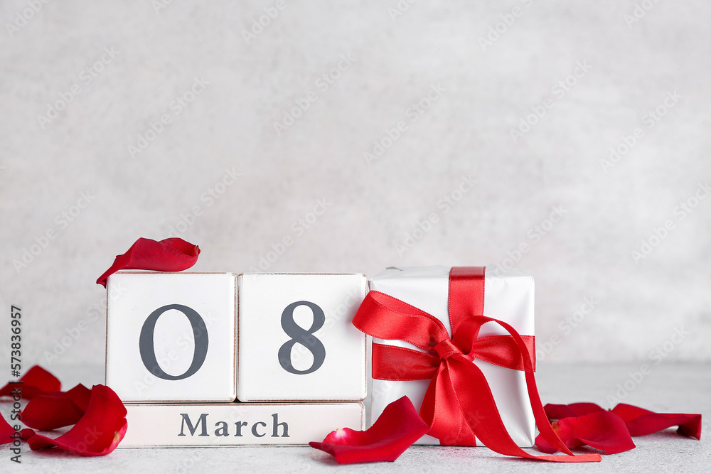 Cube calendar with date MARCH 8, gift box and rose petals on table near grey wall. Women's Day celebration