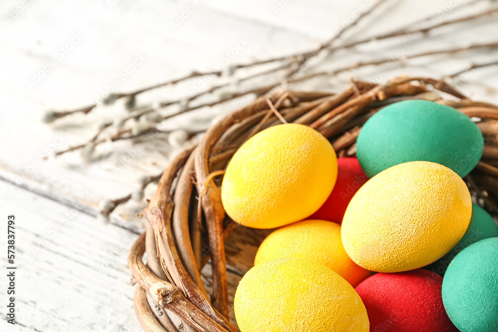 Wreath with painted Easter eggs and willow branches on light wooden ...