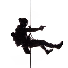 Silhouette Of Police Officer In Tactical Gear Descending From A Height, Rope Exercises With Weapons. Tactical Rappelling, Anti-terror Or Counter Terrorism Operation In Darkness In Rappelling Harness